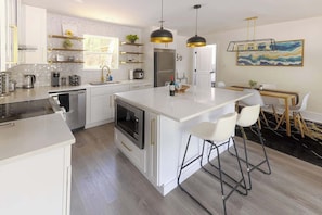 A modern kitchen with white cabinetry, a central island, bar stools, pendant lighting, and a dining area with a table and chairs.