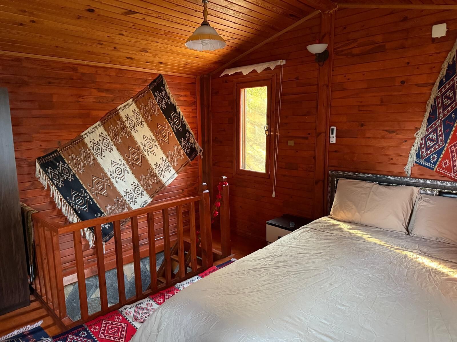 A wooden cabin room with a bed, a window, and a hanging blanket.