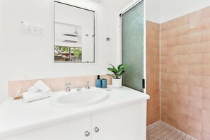 A bathroom with a white sink, mirror, and a shower area with brown tiles.