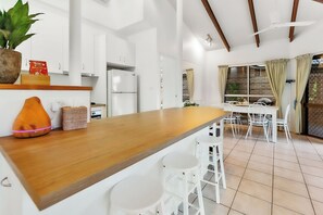 A modern kitchen with white cabinets, a wooden countertop, and a dining area with white chairs and a table.