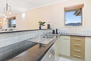 A modern kitchen with a black granite countertop, stainless steel sink, and wooden cabinets. - Stunning Mountain View Apartment - 9 Pools & Gym (Westcourt)