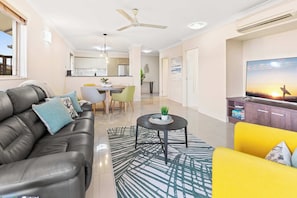 A modern living room with a sofa, a yellow armchair, a coffee table, and a TV. - Stunning Mountain View Apartment - 9 Pools & Gym (Westcourt)