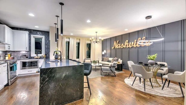 A modern kitchen with white cabinets, a marble island, and a dining area with a round table and chairs.