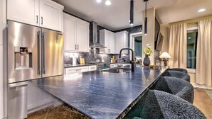A modern kitchen with stainless steel appliances, a marble countertop, and a large island with seating.