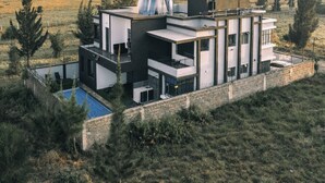 Ein modernes, mehrgeschossiges Haus mit Swimmingpool, umgeben von Bäumen und Blick auf eine entfernte Landschaft.