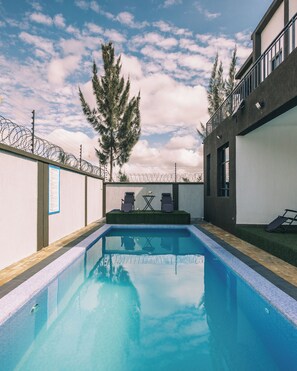Ein Swimmingpool mit Stacheldrahtzaun, zwei Liegestühlen und einem Tisch.