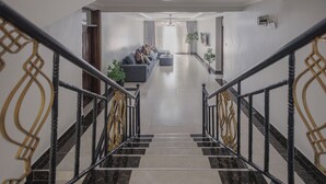 Eine moderne Hotellobby mit einer Marmortreppe, einer Sitzecke mit Sofas und einem großen Fenster mit Vorhängen.