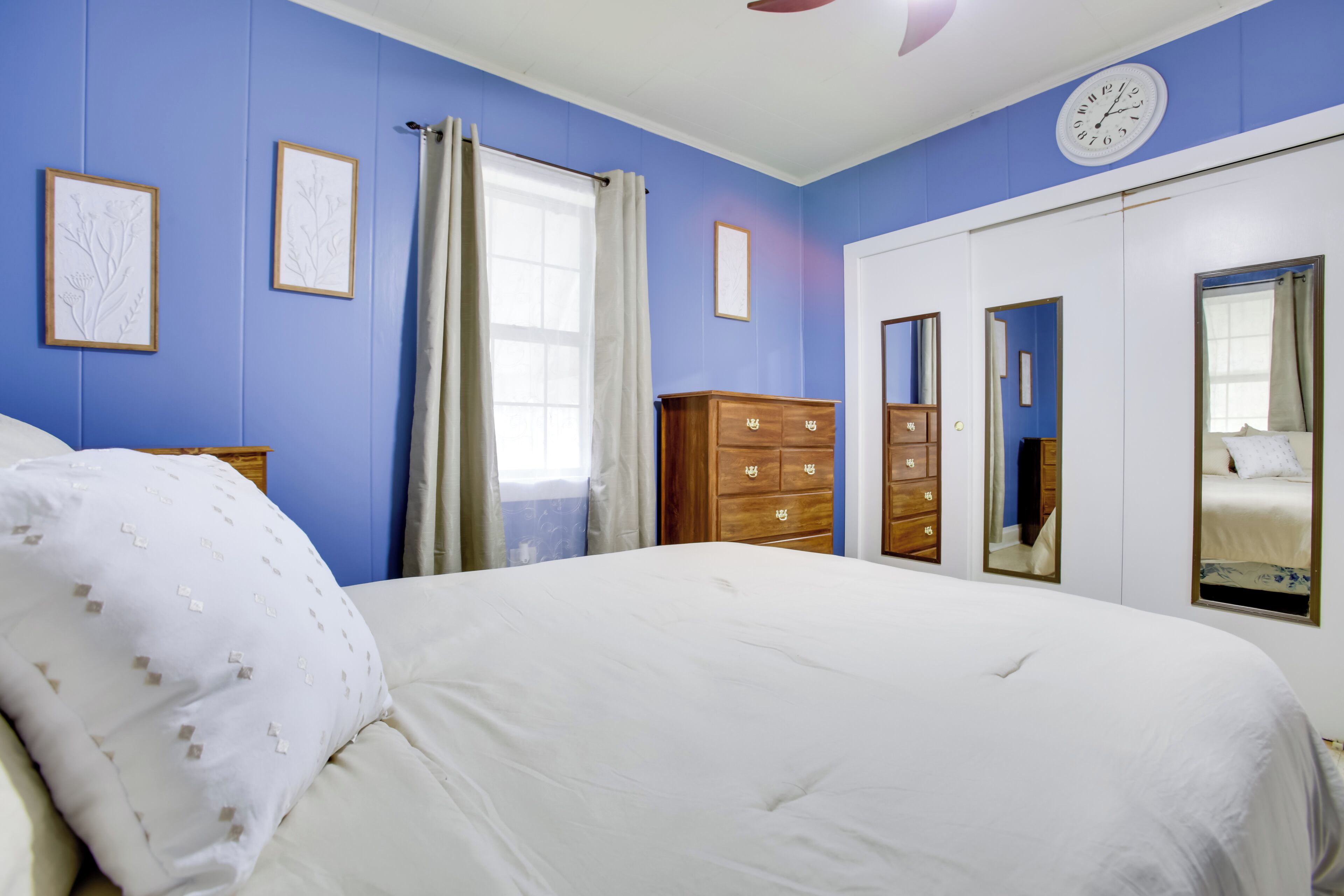 A bedroom with a bed, a dresser, a wardrobe, and a clock on the wall.