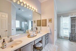A bathroom with a large vanity, a mirror with lights, a sink, and a toilet.