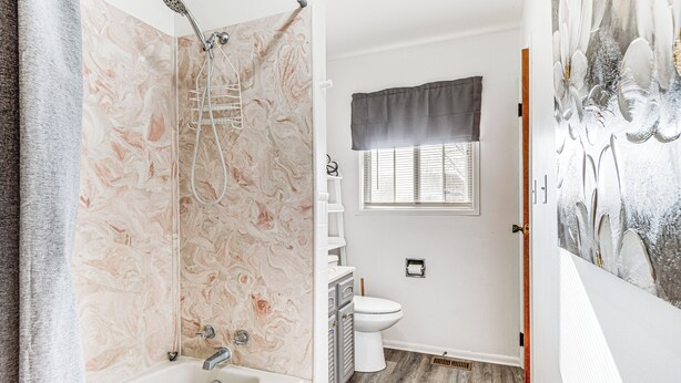 Un baño con pared de ducha de mármol, bañera, inodoro y ventana con cortina.