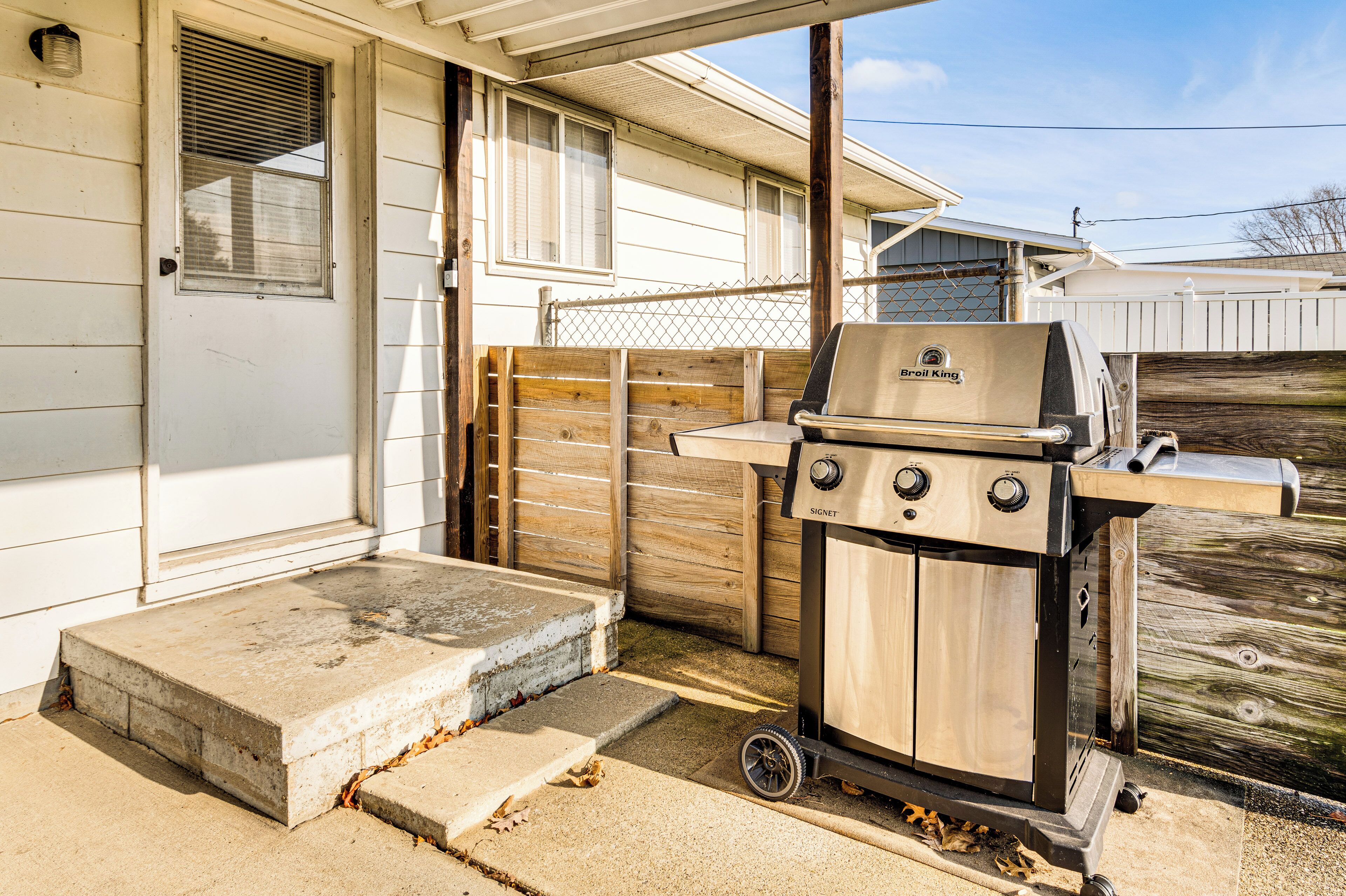 A portable grill with wheels, a concrete step, and a wooden fence in front of a house.