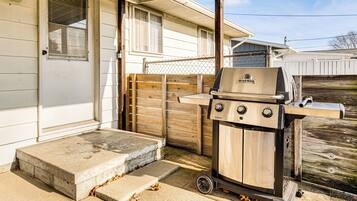 A portable grill with wheels, a concrete step, and a wooden fence in front of a house.