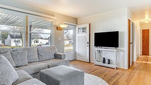 A living room with a sectional sofa, a flat-screen TV on a white entertainment unit, and large windows offering a view of the outside. - 2 Mi to Downtown Logansport: Quiet Home w/ Grill (Logansport)