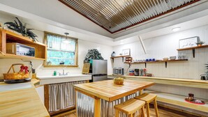Een keuken met een houten tafel, barstoelen, een koelkast en diverse keukenapparaten.