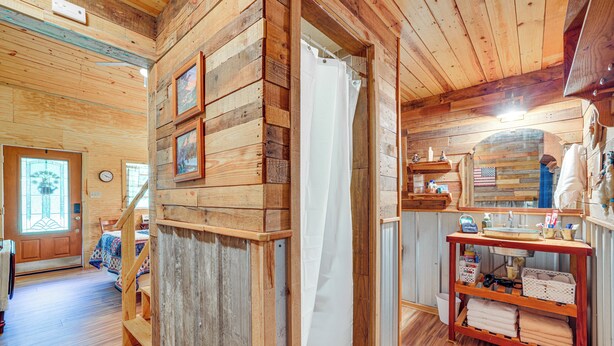 Interieur van een houten hutje met een trap, een badkamer met douchegordijn en een plank met handdoeken.