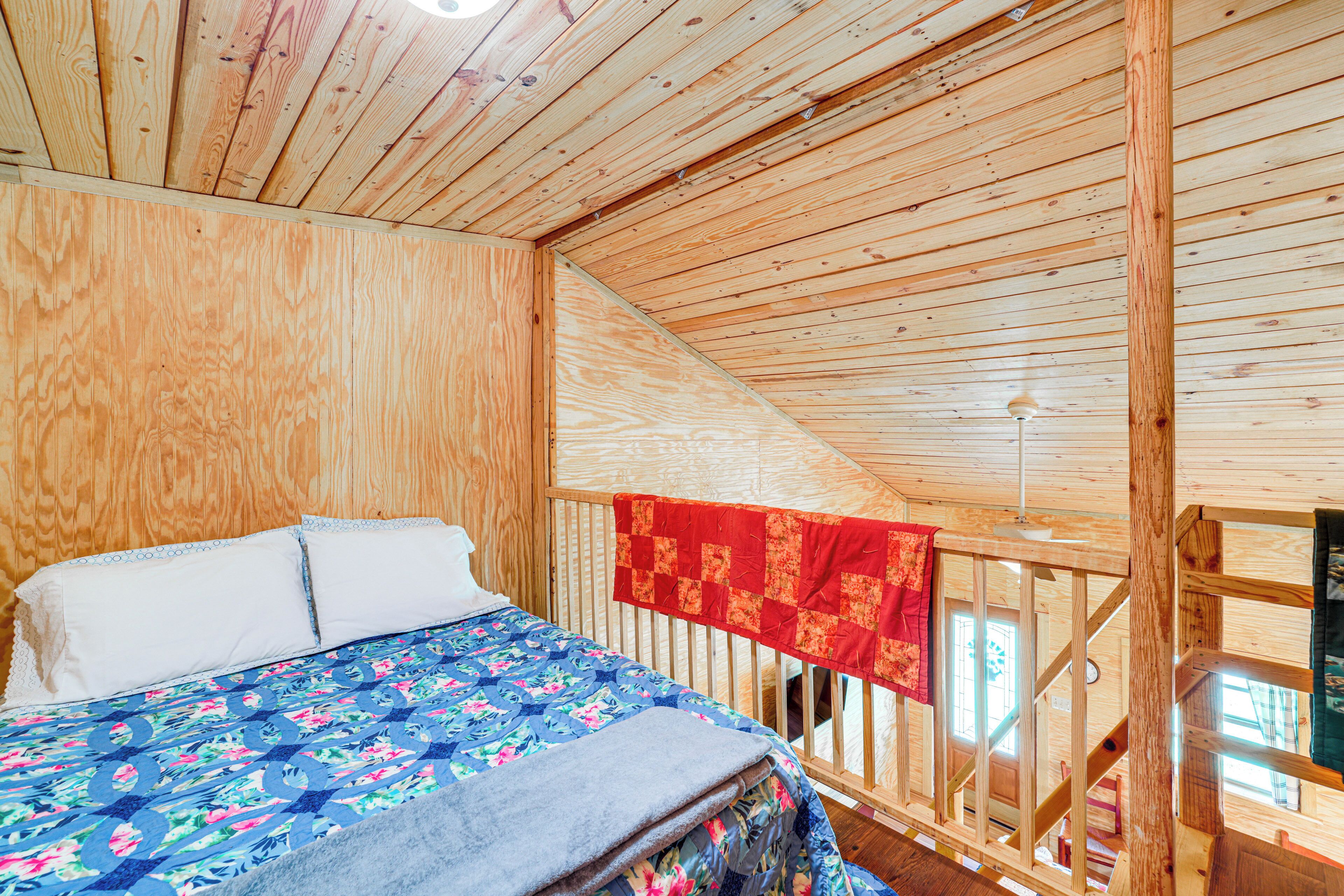 A wooden cabin room with a bed, a red quilt, and a wooden railing.