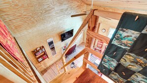 Een houten interieur met een trap, een televisie en een quilt aan de muur.