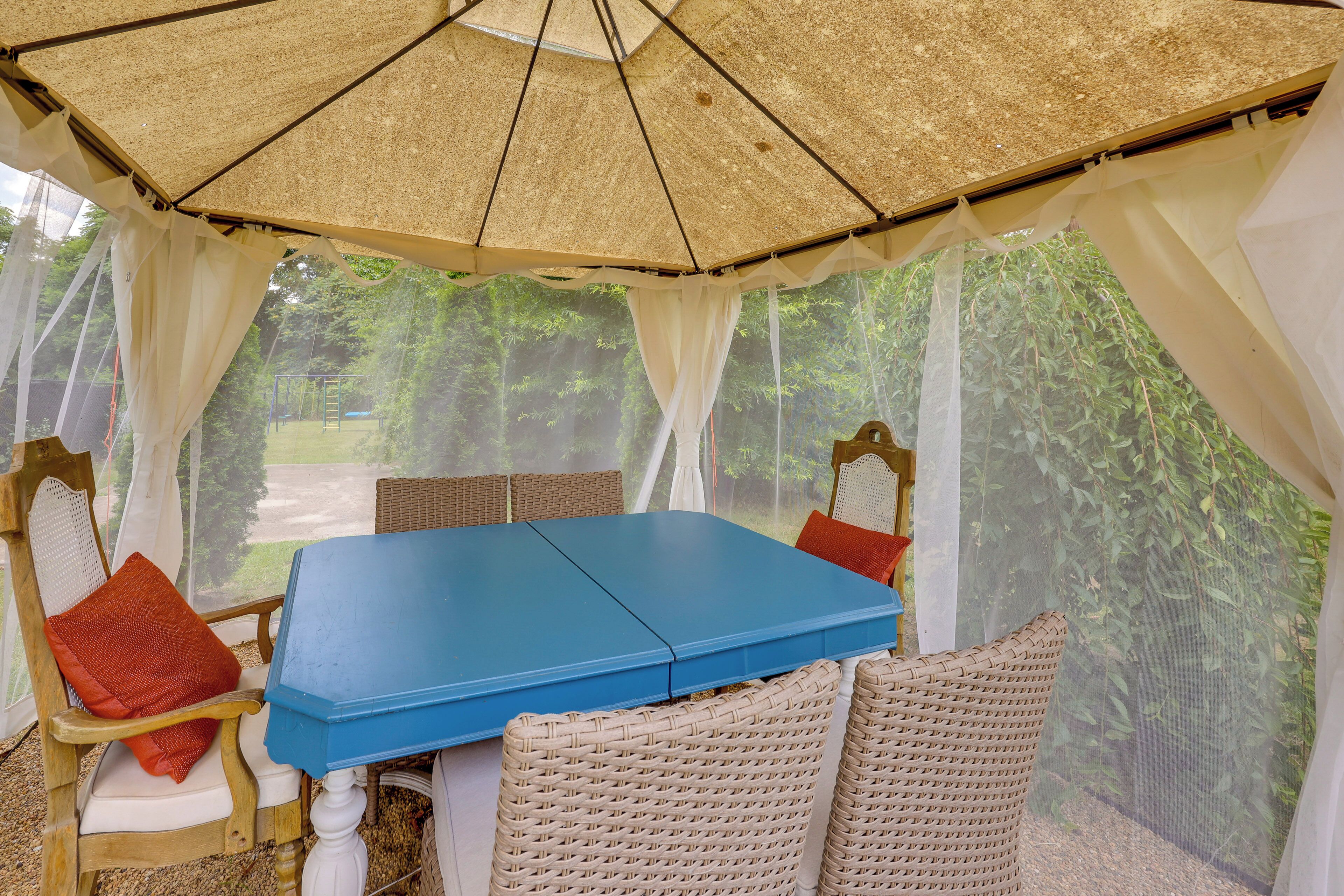 Un espace extérieur aménagé avec des sièges, protégé par un auvent, comprenant une table et des chaises, le tout entouré de rideaux blancs et agrémenté d’un décor naturel.