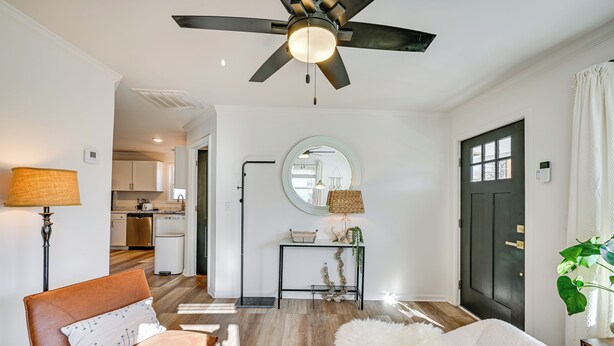 A modern living room with a ceiling fan, a sofa, a chair, and a coffee table. There is a kitchen in the background with cabinets and a countertop. - < 3 Mi to Dtwn: Modern Cottage in Greenville! (Greenville)