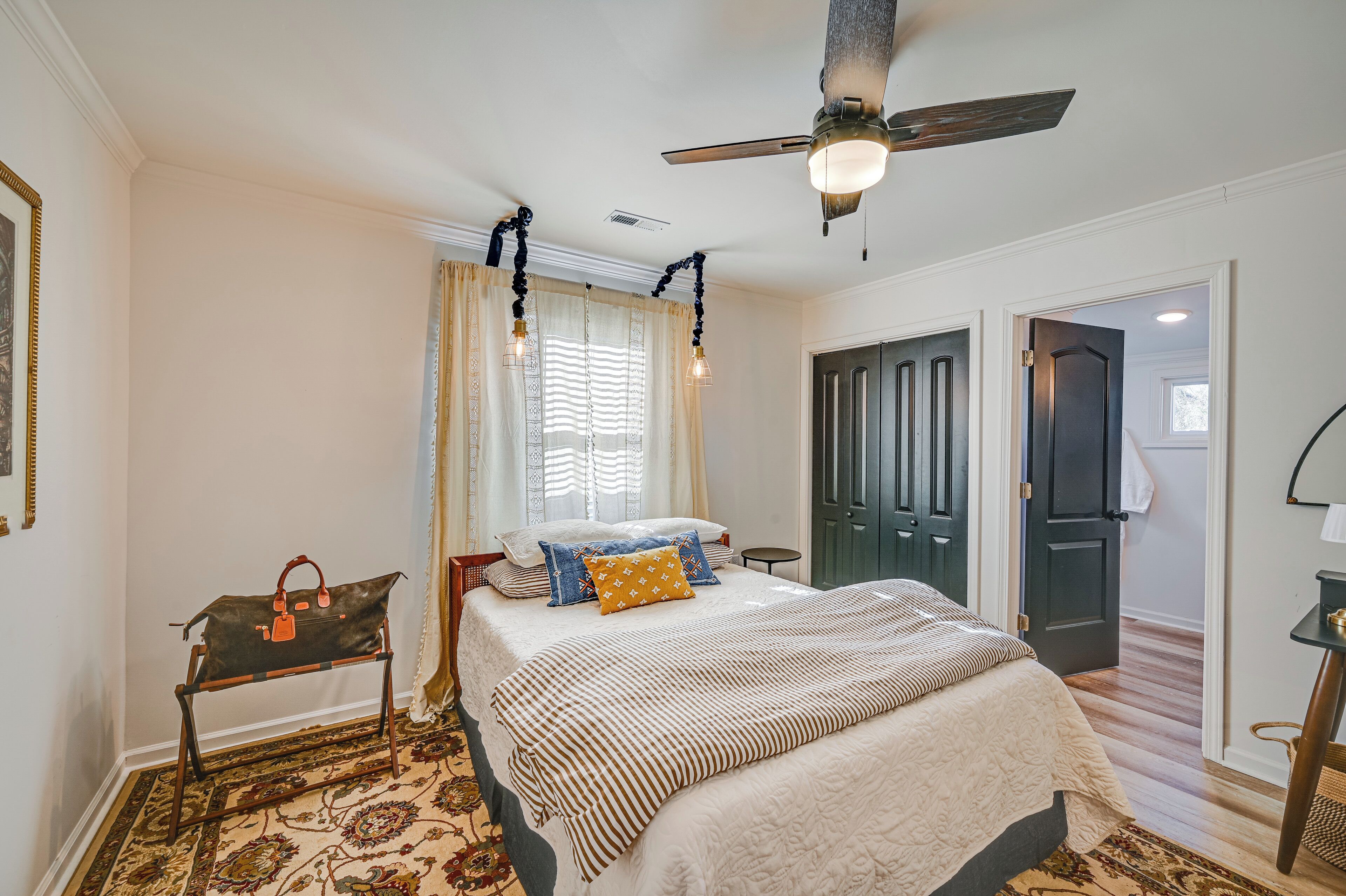A bedroom with a bed, a standing lamp, a ceiling fan, and a door leading to another room.
