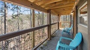 A wooden deck with a railing, two blue chairs, and a view of trees. - New! Bring Pets! Firepit*Fishing*Games*Sleeps 5! (Sevierville)