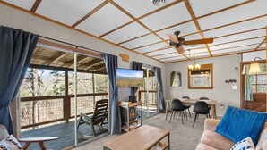 A cozy cabin interior with a wooden ceiling, a fireplace, a dining area, and a large window offering a scenic view. - New! Bring Pets! Firepit*Fishing*Games*Sleeps 5! (Sevierville)