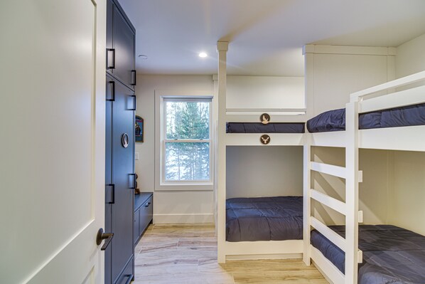A bedroom with bunk beds, a wardrobe, and a window with a view of trees. - Mtn Escape w/ Hot Tub, By Trails in Grand Lake! (Grand Lake)