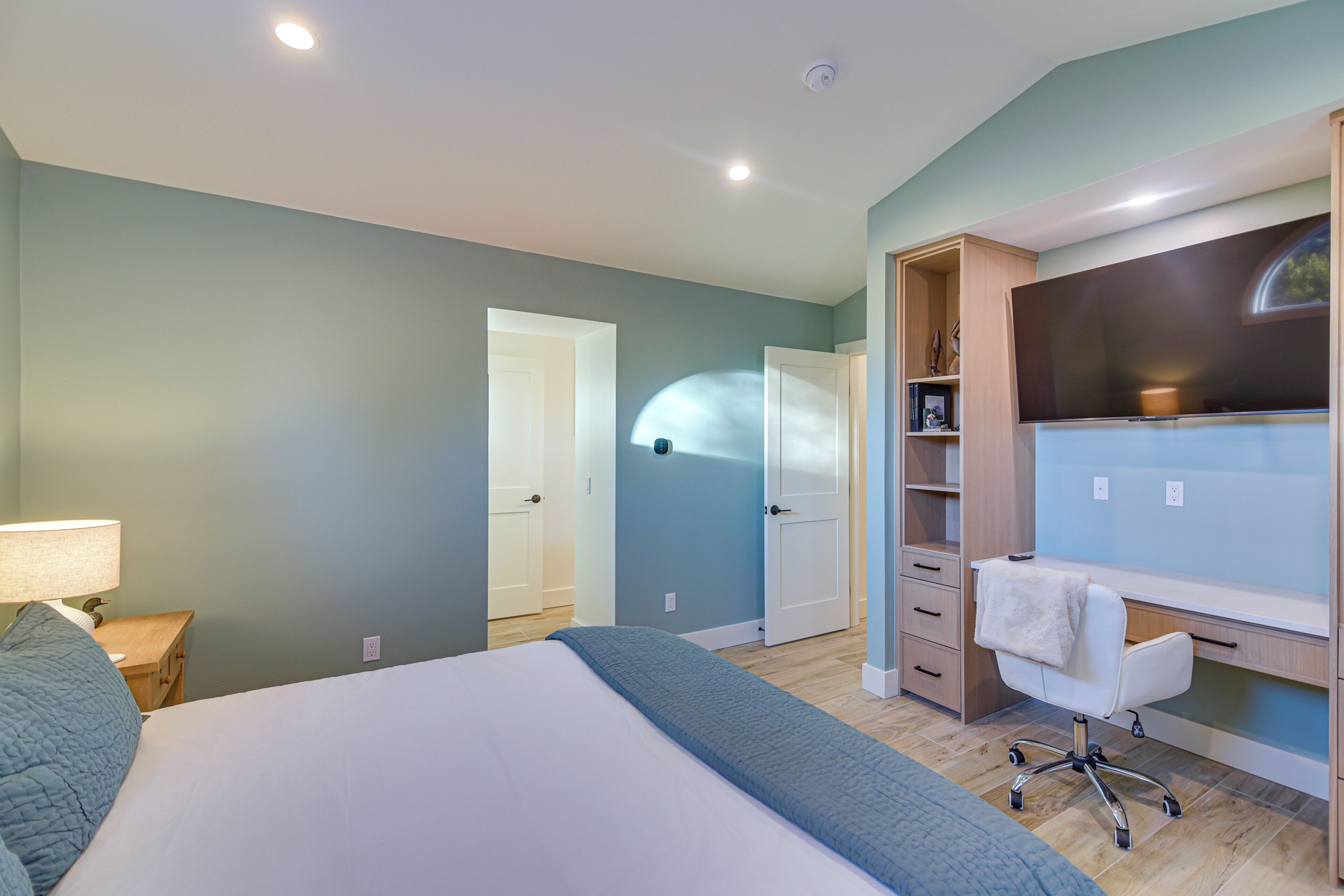 Une chambre à coucher avec un lit, un bureau et une chaise. Une porte donne accès à une autre pièce.
