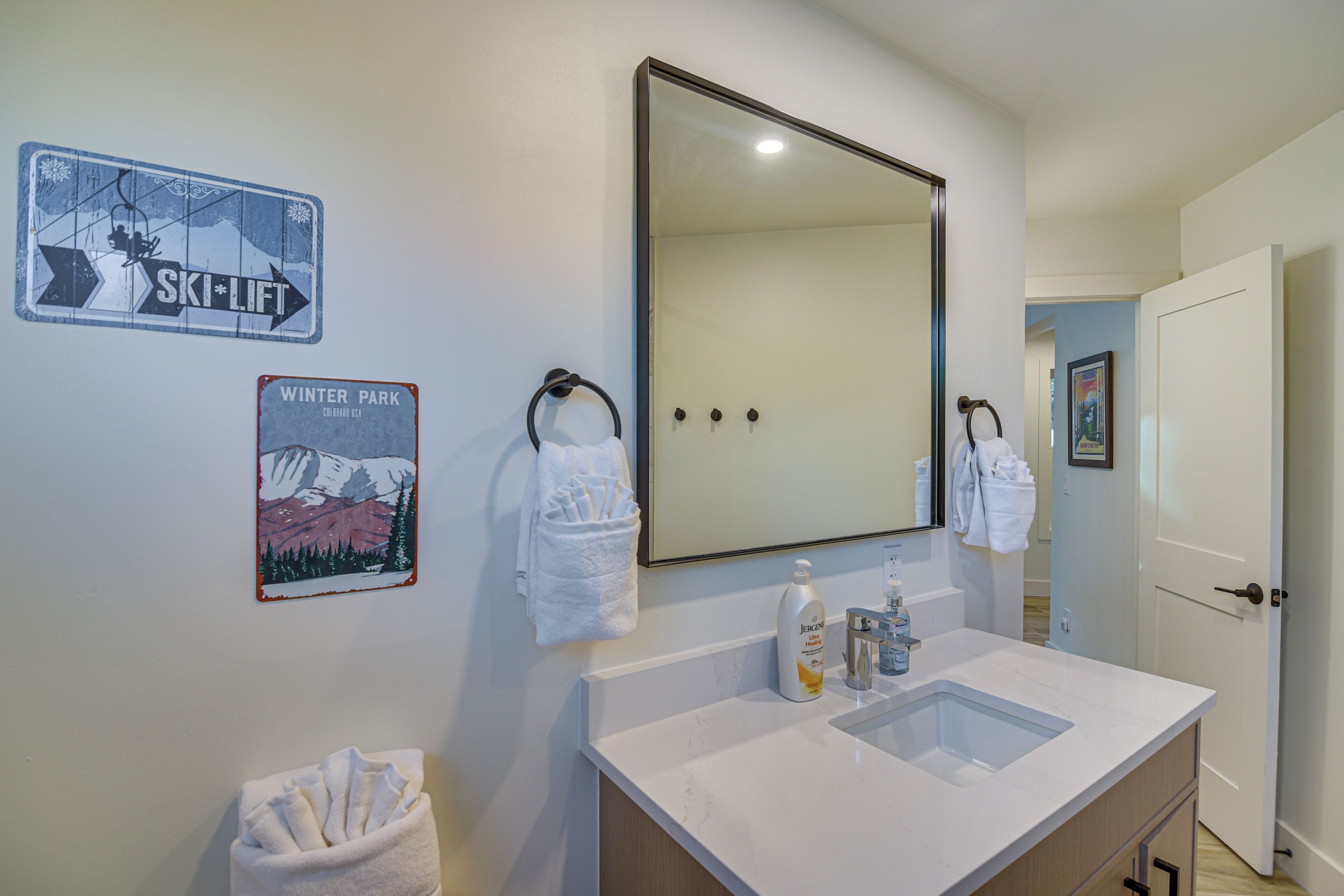 A bathroom with a large mirror, a sink, and two towels hanging on hooks. There are signs on the wall indicating a ski lift and a winter park.