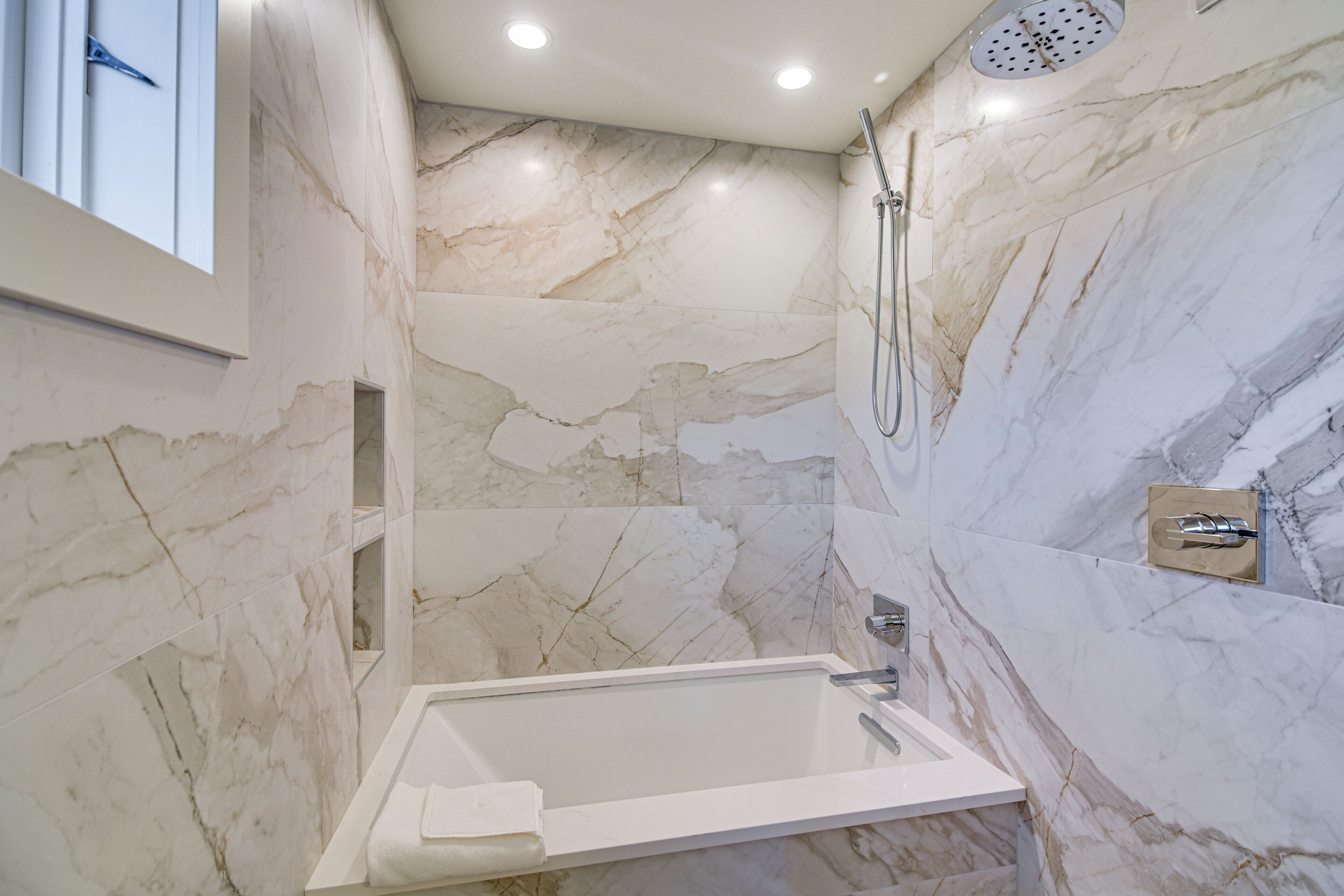Een moderne badkamer met een marmeren wand, een badkuip en een douche.