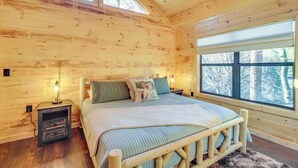 Un dormitorio de cabaña de madera con una cama, mesitas de noche y un ventanal grande.