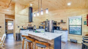 Una cocina moderna con paredes de madera, una isla de mármol, taburetes de bar y electrodomésticos de acero inoxidable.