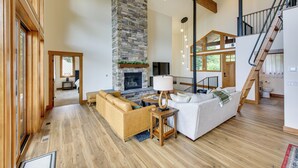 A spacious living room with a stone fireplace, wooden floors, and a staircase leading to an upper level. - Stunning View! Peaceful & Modern Schweitzer Chalet (Sandpoint)