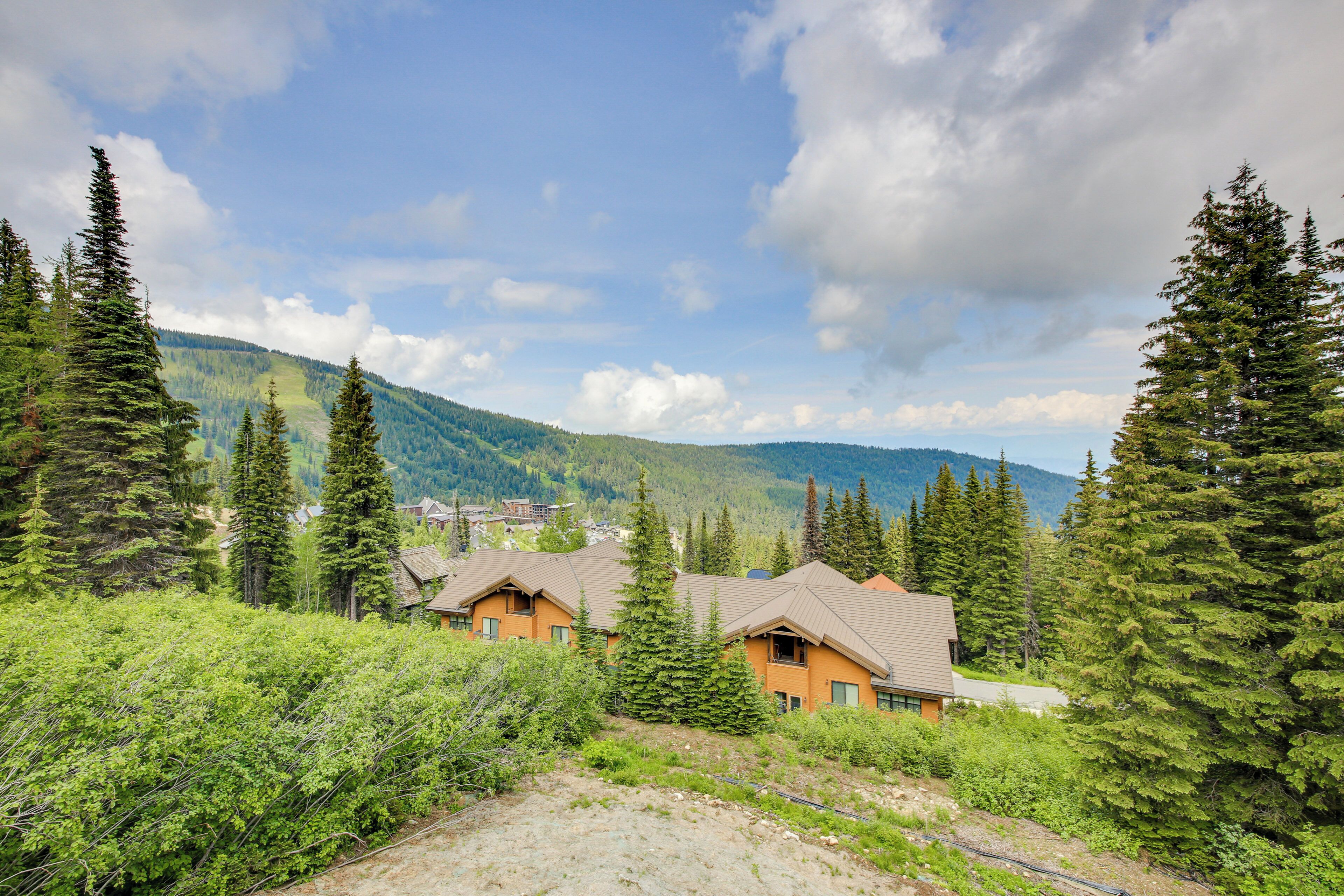 Un albergue de montaña con varias cabañas rodeado de un bosque denso y montañas al fondo.