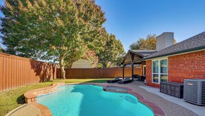 A backyard with a swimming pool, a wooden fence, and a brick building. - Outdoor Oasis w/ Pool: Grand Prairie Family Home! (Grand Prairie)