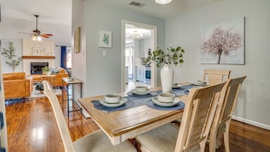 A dining area with a wooden table set for four, surrounded by wooden chairs. A vase with green plants is on the table. - Outdoor Oasis w/ Pool: Grand Prairie Family Home! (Grand Prairie)