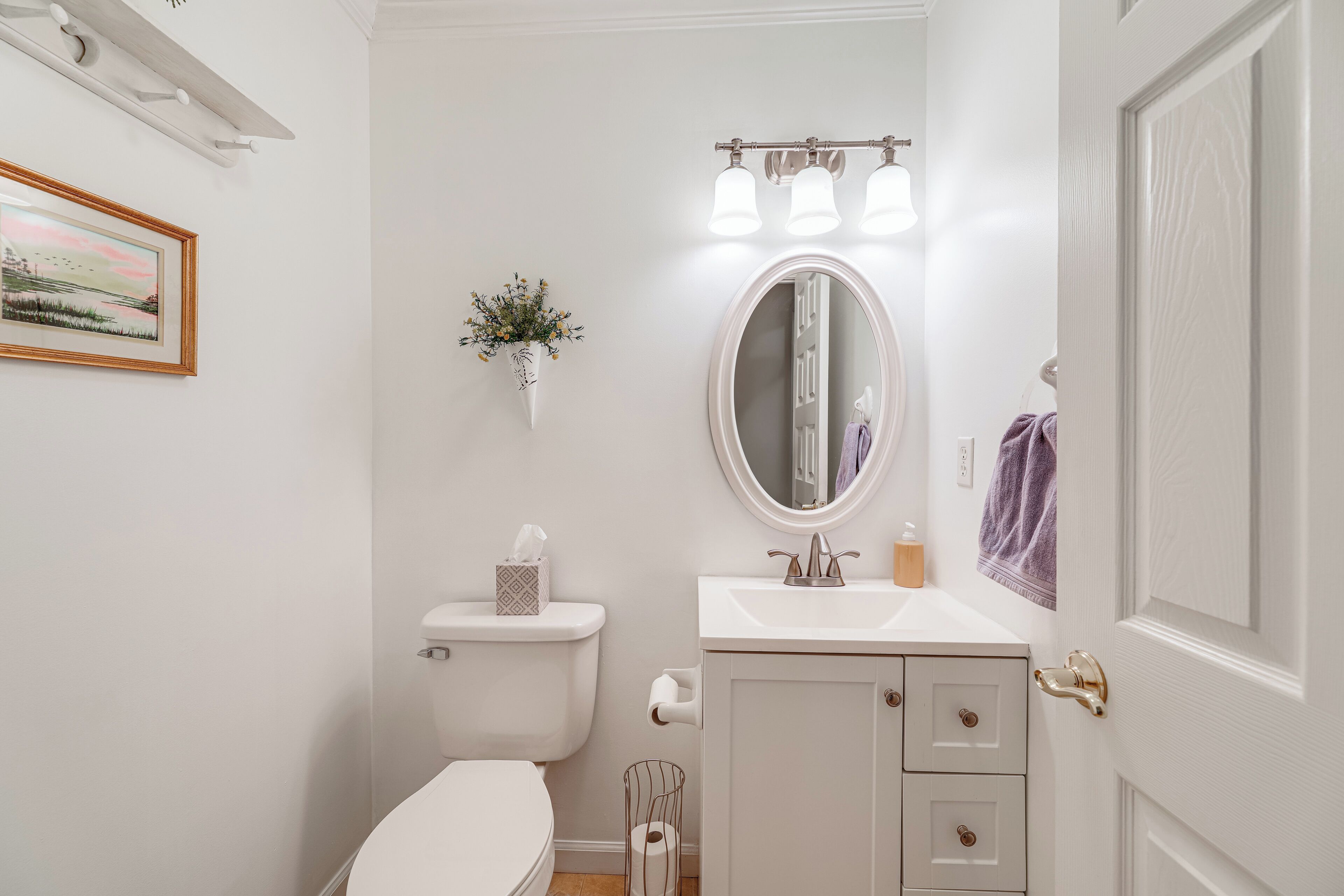 A bathroom with a toilet, sink, mirror, and a small trash bin.
