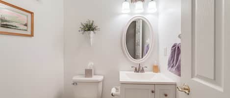 A bathroom with a toilet, sink, mirror, and a small trash bin.