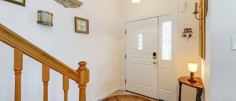 A hallway with a wooden staircase, a white door with a glass window, a round carpet, and a small table with a lamp.