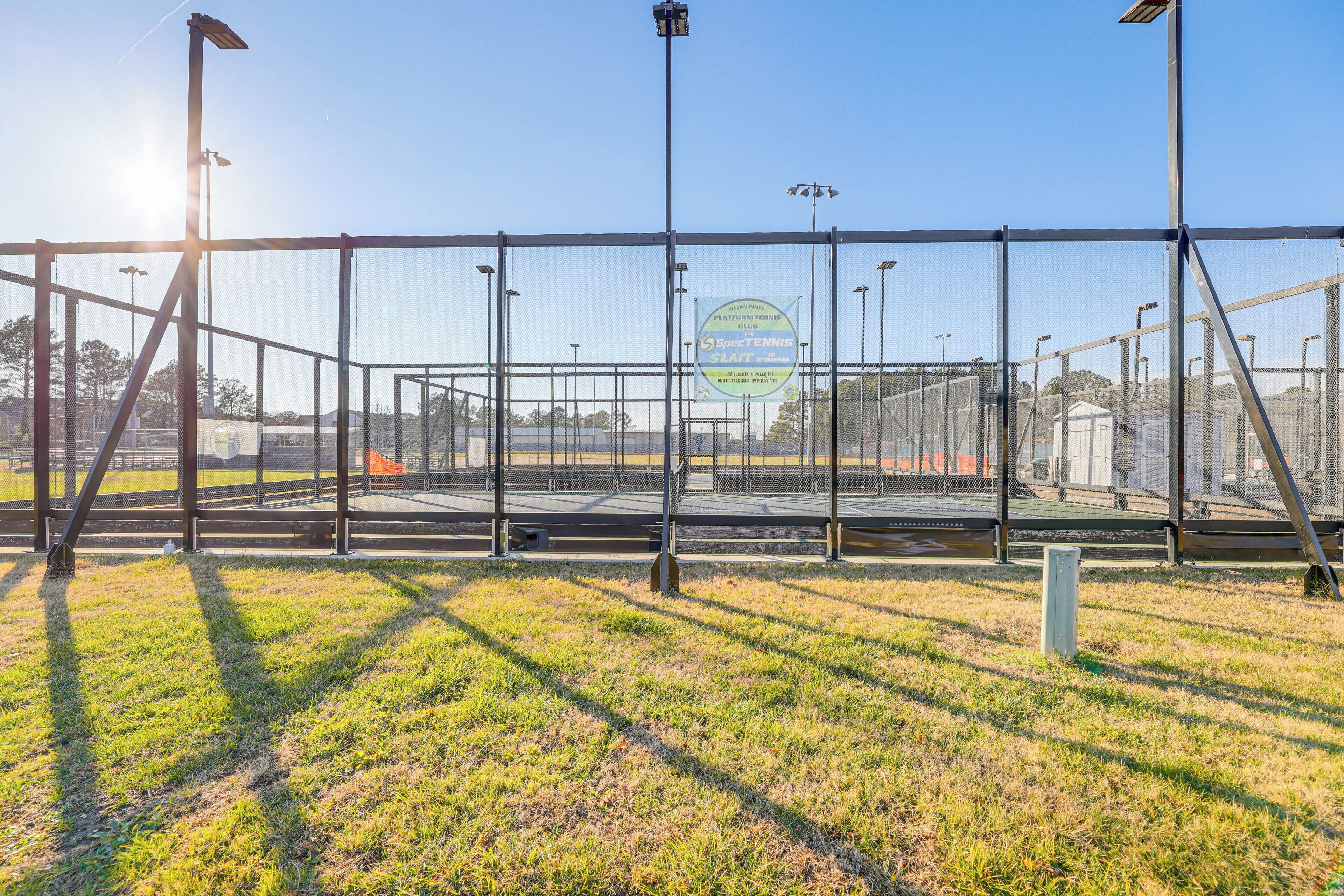 Una cancha de tenis con cerca metálica, luces solares y cielo despejado.
