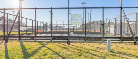 Una cancha de tenis con cerca metálica, luces solares y cielo despejado.