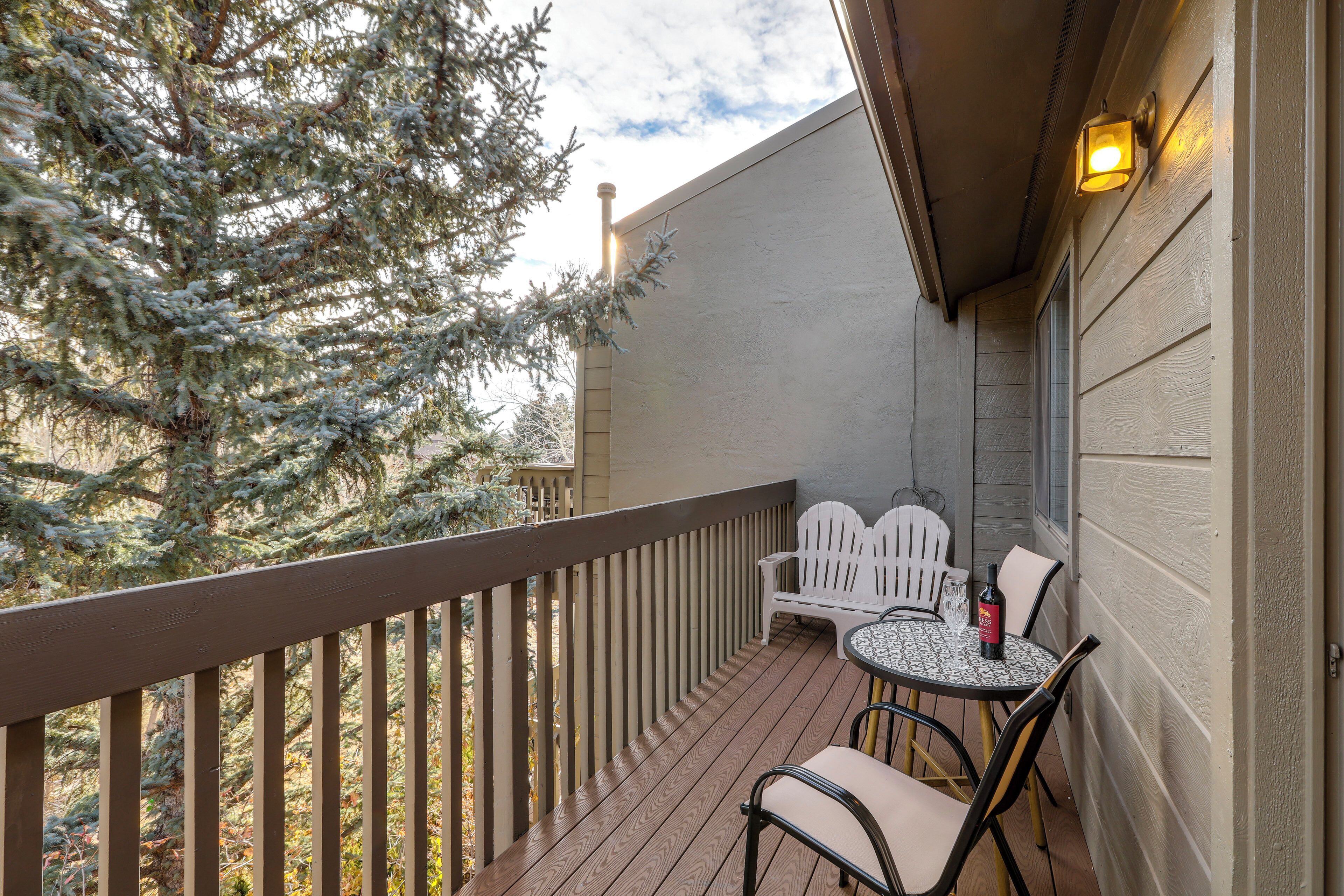 A wooden deck with a white chair and table, a potted plant, and a tree with snow on its branches.