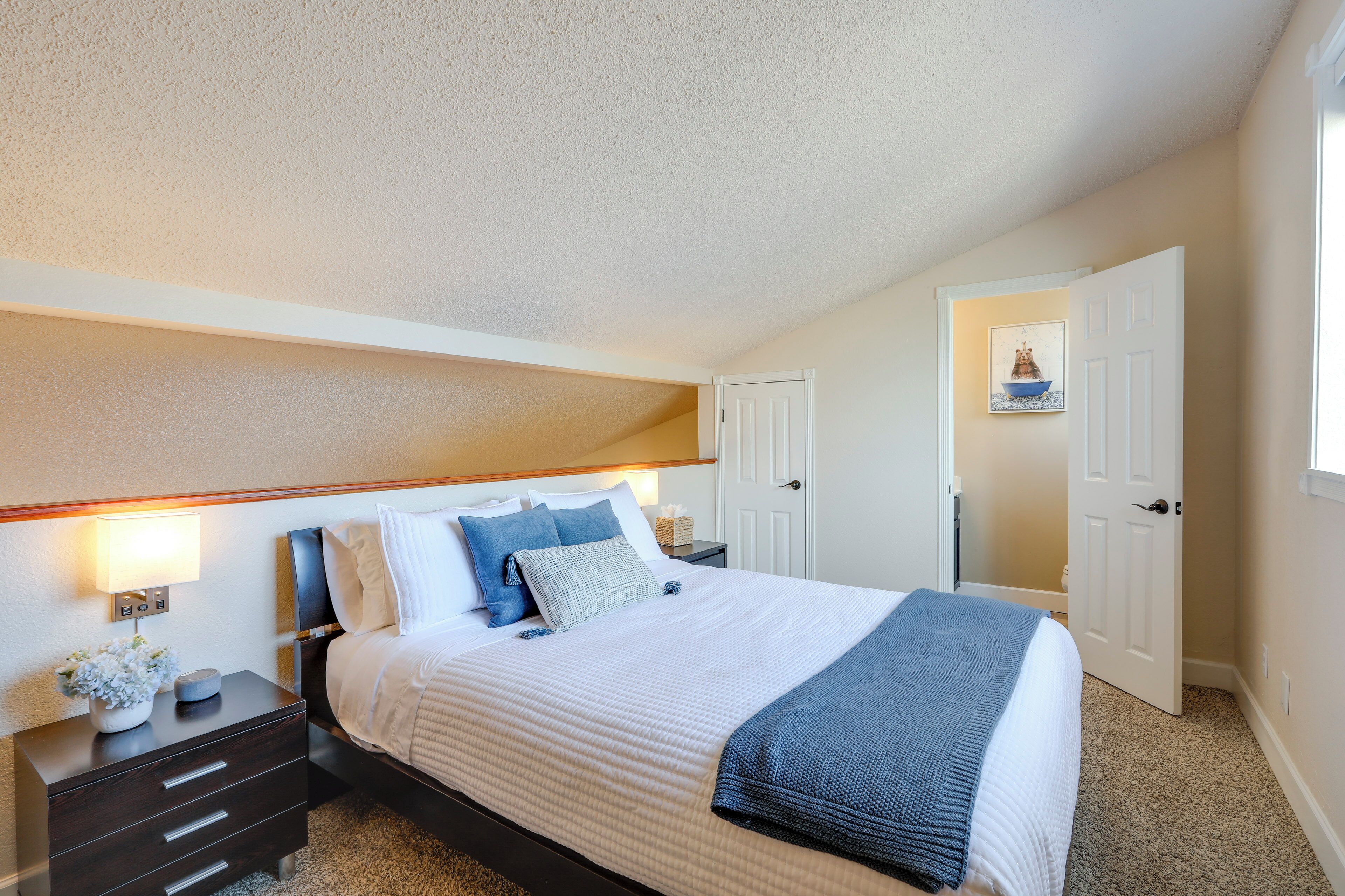 A bedroom with a bed, bedside tables, a nightstand, a lamp, and a picture frame on the wall.