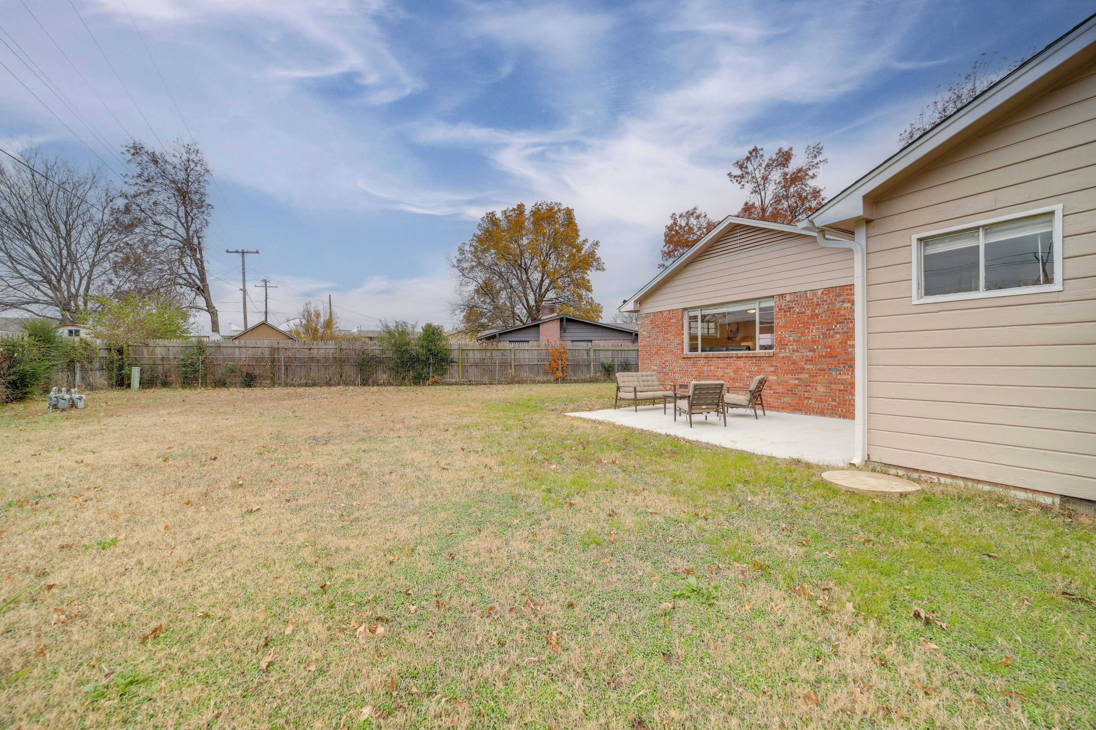 A backyard with a patio area, a brick building, and a wooden fence.