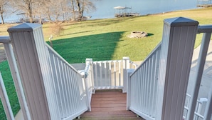 A wooden staircase with white railings leading to a grassy area with a dock and a body of water in the background.