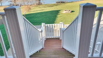 Una escalera de madera con barandillas blancas que conduce a una zona cubierta de césped, con un muelle y una masa de agua al fondo.