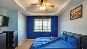 A bedroom with a bed, a ceiling fan, a window, a painting, and a TV.