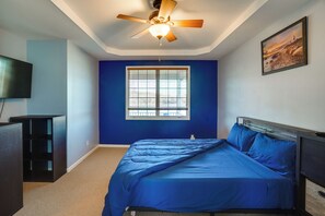 Ein Schlafzimmer mit Bett, Deckenventilator, Fenster, Gemälde und Fernseher.