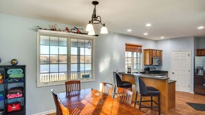A spacious kitchen with a large island, wooden dining table, and a view of the outdoors through a large window.