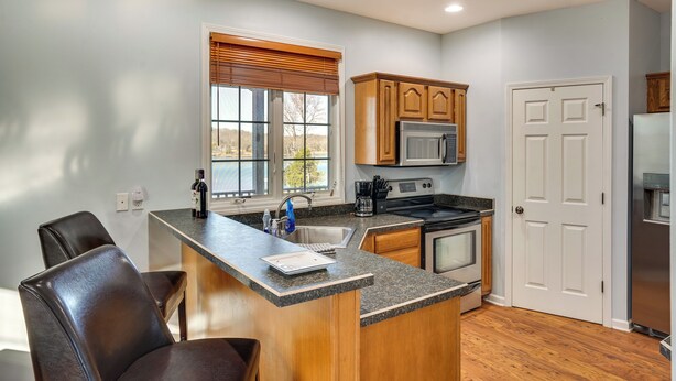 A kitchen with wooden cabinets, a granite countertop, a built-in microwave, and a stainless steel refrigerator.